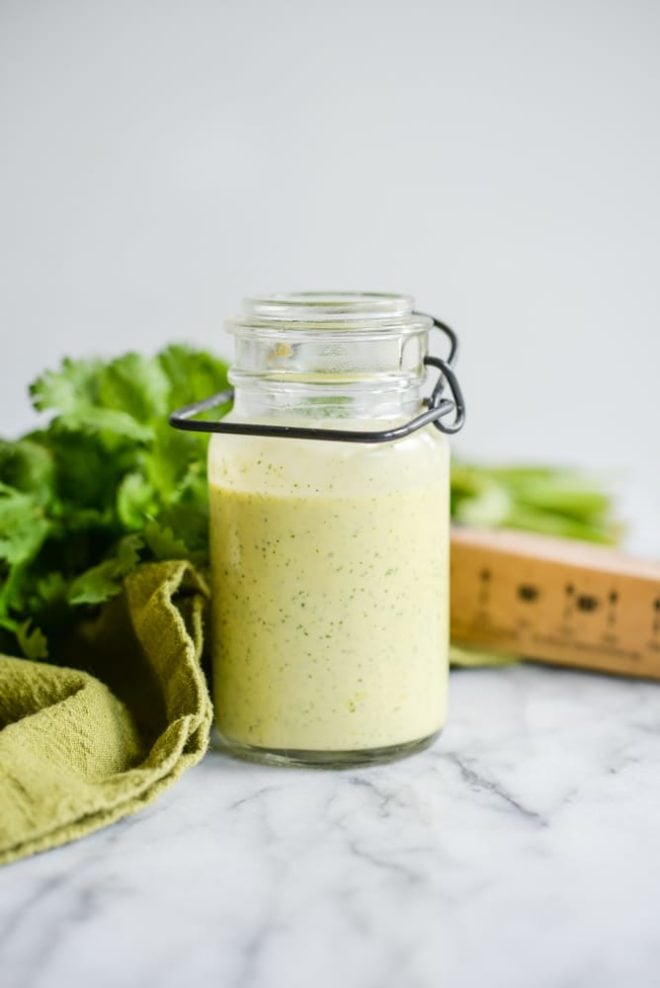 glass jar of cilantro hollandaise sauce on a white marble table with cilantro in the background