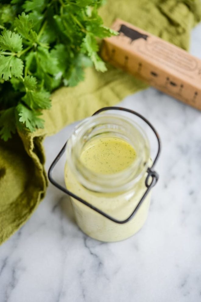 glass jar of cilantro hollandaise sauce on a white marble table with cilantro in the background