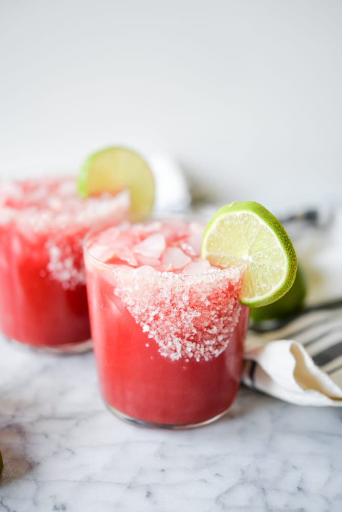 bright pink ginger beet margaritas in a glass with salt on the rim and a circle of lime on a marble surface