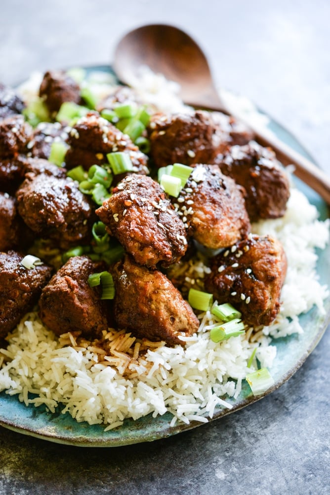 turkey teriyaki meatballs on a bed of rice on a blue plate with a wooden serving spoon