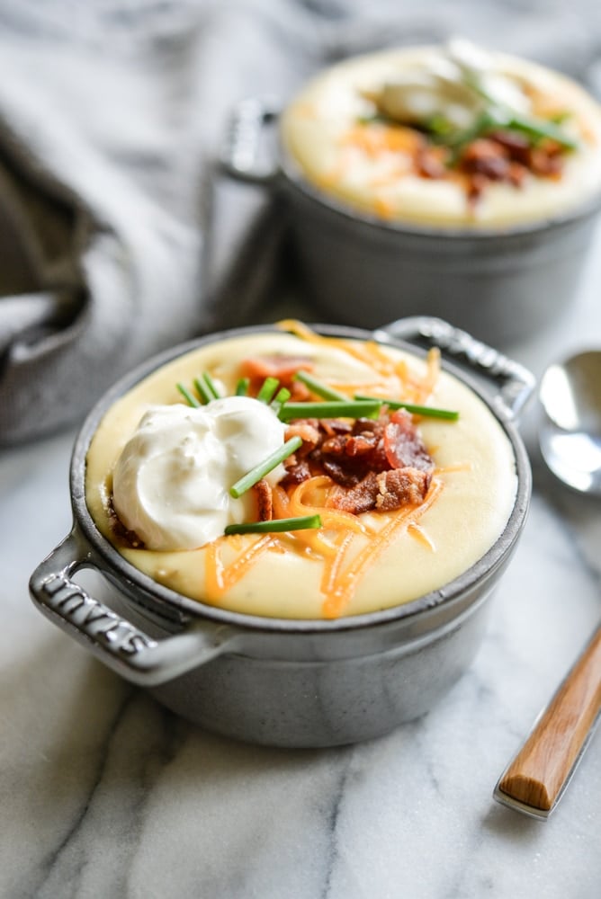 instant pot loaded potato soup in a grey cast iron pot with sour cream, bacon, cheese, and chives on top
