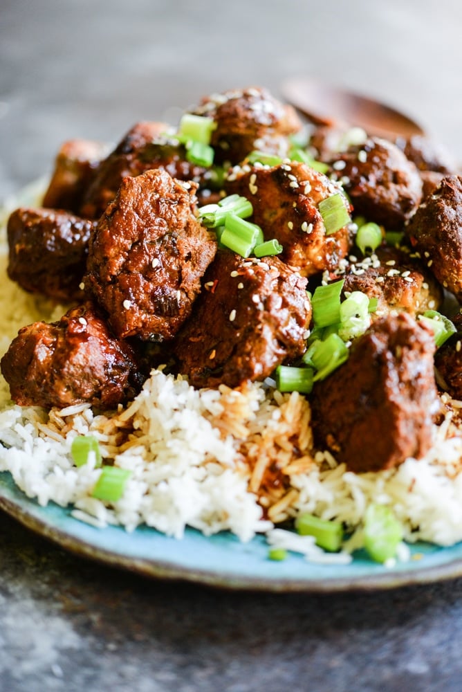 turkey teriyaki meatballs on a bed of rice on a blue plate on a dark grey surface