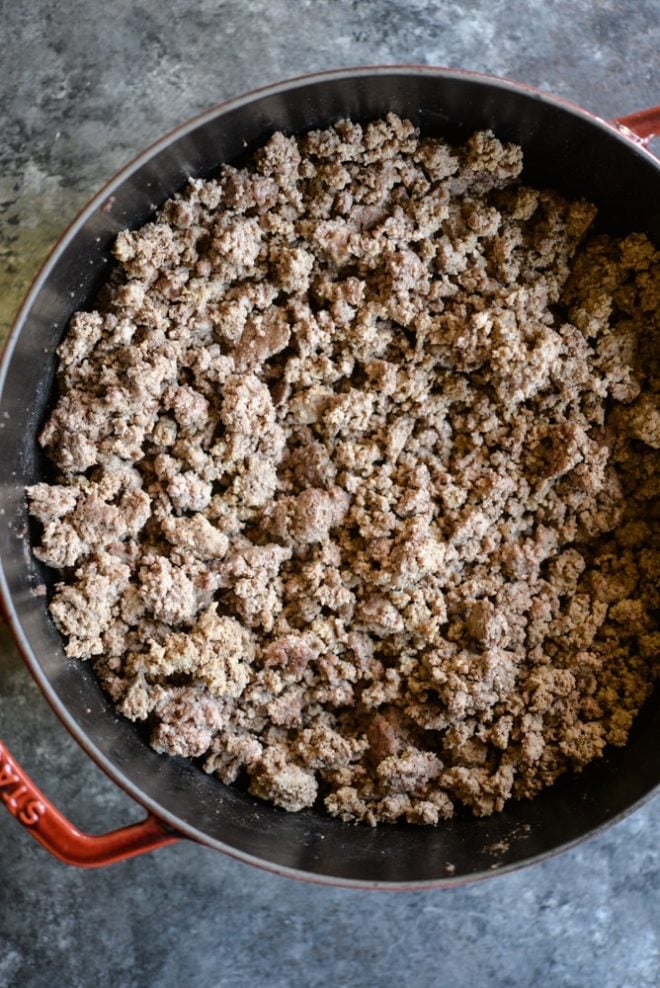 ground beef in a red cast iron pan on a dark grey surface