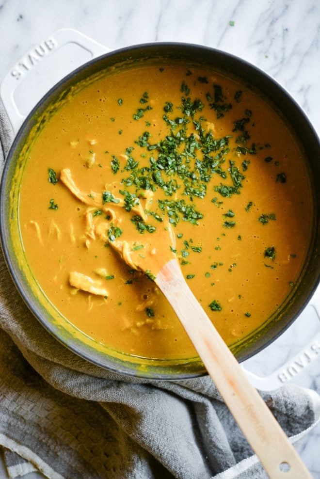 meal prep Curried Butternut Squash Soup in a cast iron pot being stirred by a wooden spoon