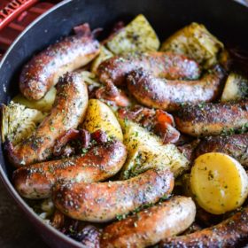 browned sausages, halved gold potatoes, and cabbage wedges in a large red cast iron duch oven on a dark grey surface - dublin coddle