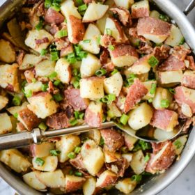 german potato salad with diced red potatoes, green onions, and bacon in a stainless steel skillet on a marble surface