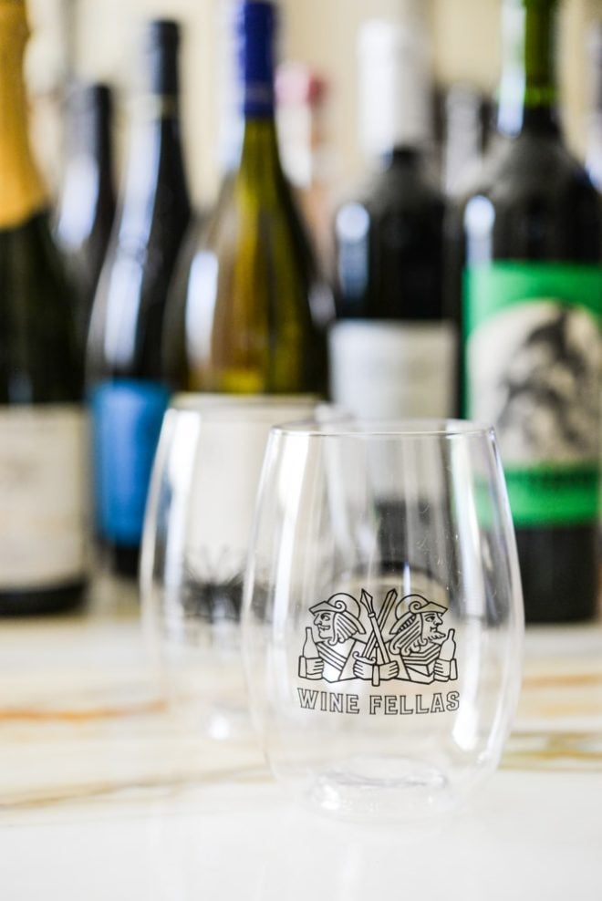 a wine fellas stemless wine glass with assorted natural wine bottles in the background