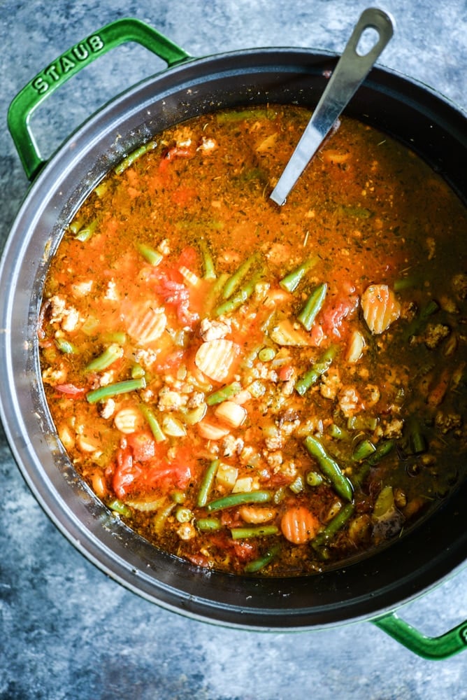 bright red paleo minestrone soup in a green cast iron pot on a dark grey board