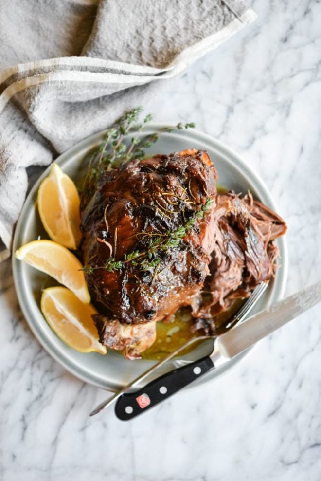 Slow Roasted Leg of Lamb on serving plate with orange slices, fork, and knife