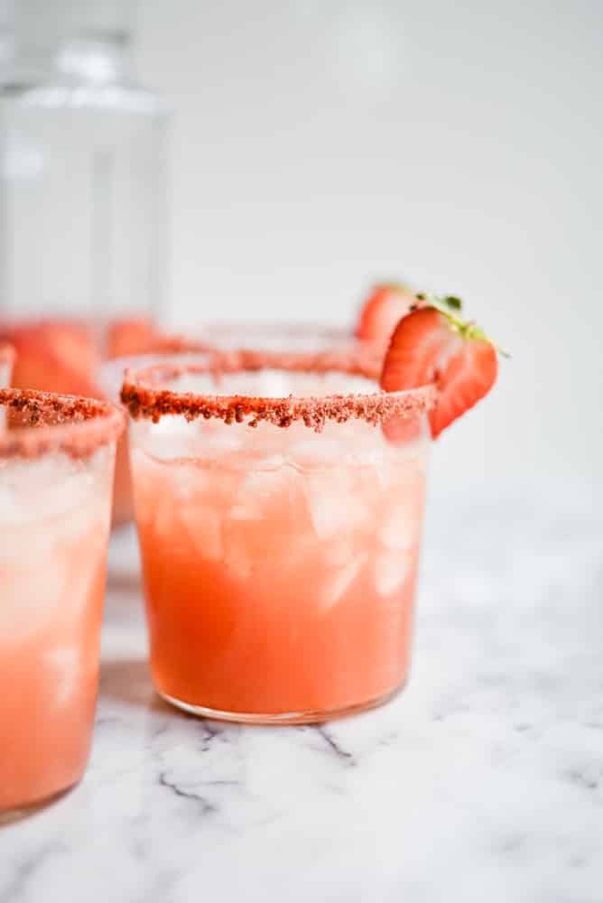 pink sangria in a glass with a powdered strawberry rim and a strawberry slice on a marble surface