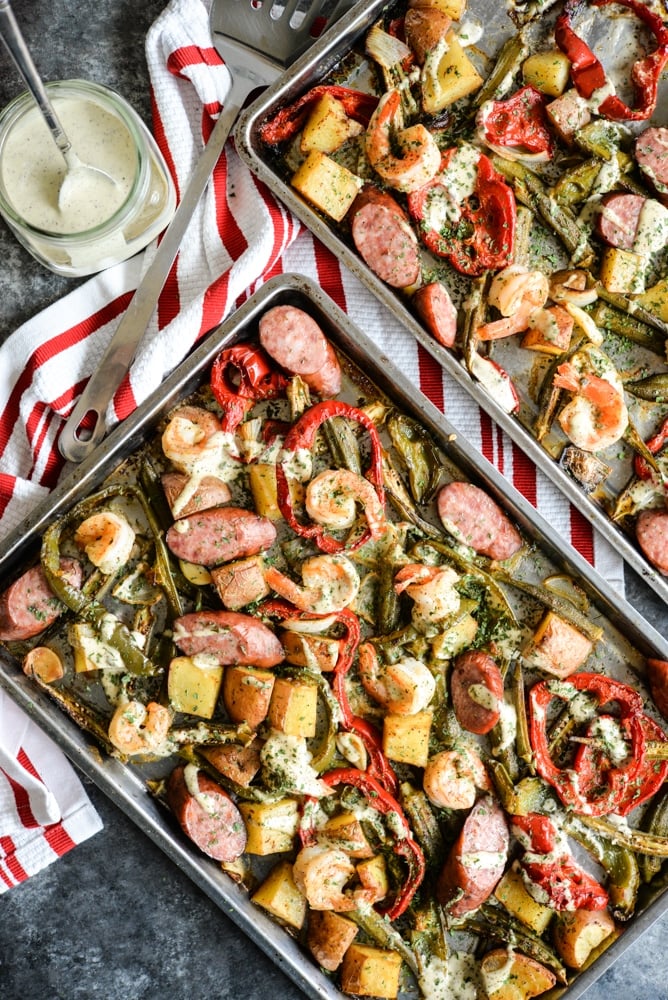 cajun sheet pan dinner with shrimp, sausage, bell peppers, red potatoes, and okra with a creamy remoulade sauce drizzled on top