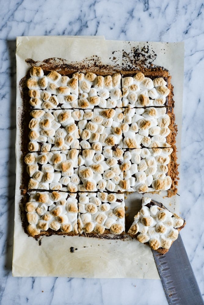 smores bars with toasted marshmallows on top on parchment paper on a marble surface