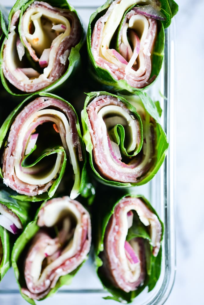 close up shot of collard green wraps filled with meat and cheese in a glass container on a marble surface