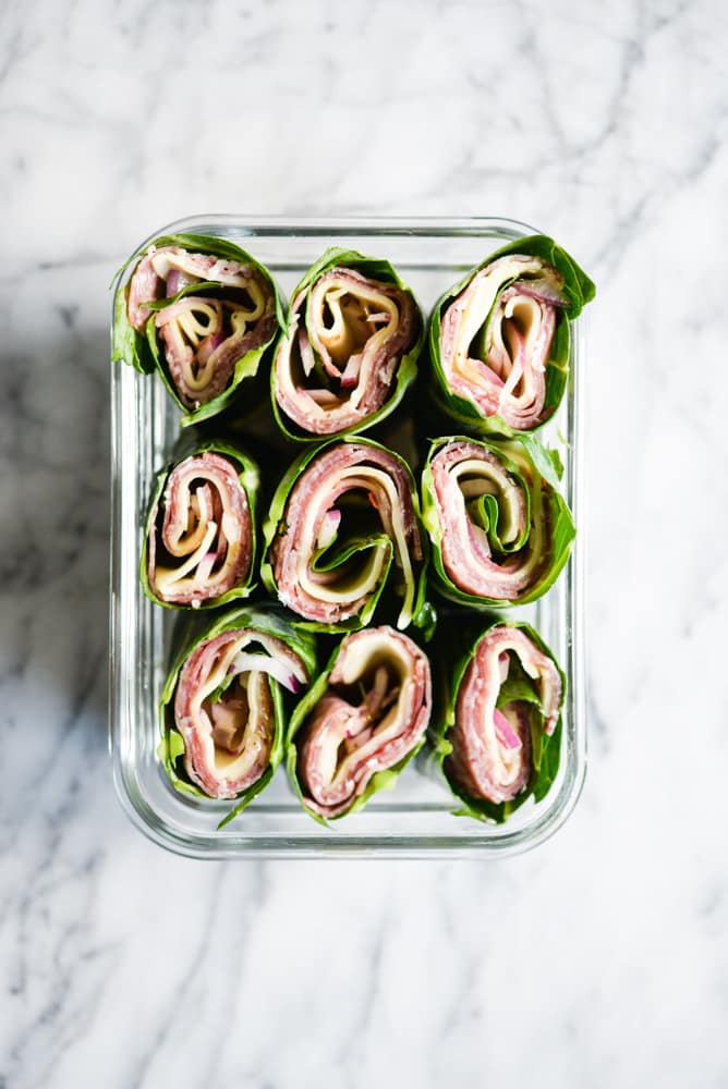 collard green wraps filled with meat and cheese in a glass container on a marble surface