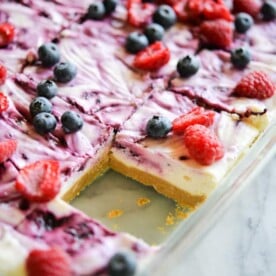 These no-bake berry cheesecake bars are a decadent dessert that are a serious crowd-pleaser! A simple gluten free graham cracker crust is topped with a luscious cheesecake filling, then swirled with a fresh berry sauce made with blueberries, raspberries, and blackberries. After a quick chill in the fridge, simply cut into squares and serve! The best part about these no-bake berry cheesecake bars is that they can be easily modified to be dairy free and paleo!