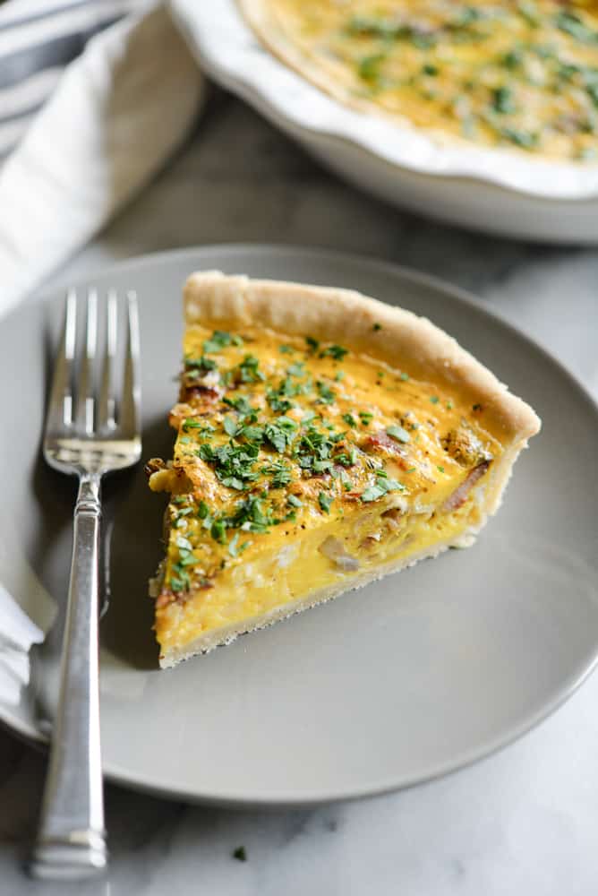 a slice of gluten-free quiche on a grey plate with a silver fork on a marble surface