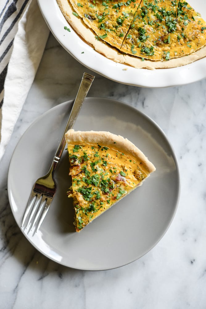 a slice of gluten-free quiche on a grey plate with a silver fork on a marble surface