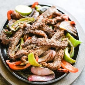 plate of sizzling beef fajitas with grilled red and green bell peppers and red onions