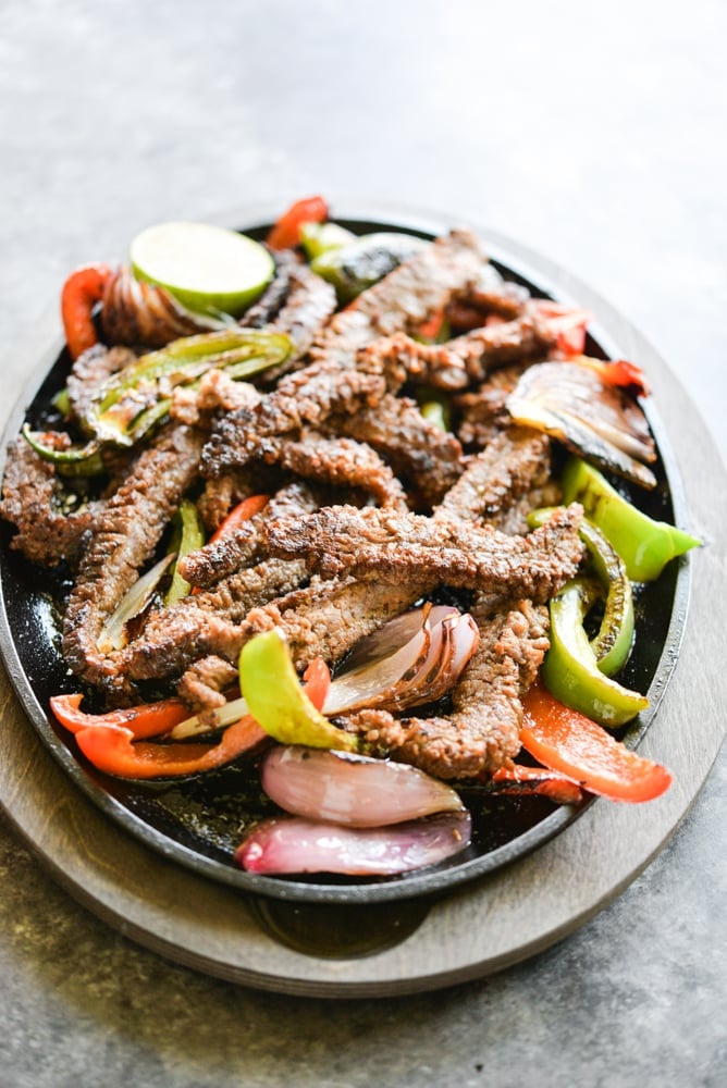 plate of sizzling beef fajitas with grilled red and green bell peppers and red onions
