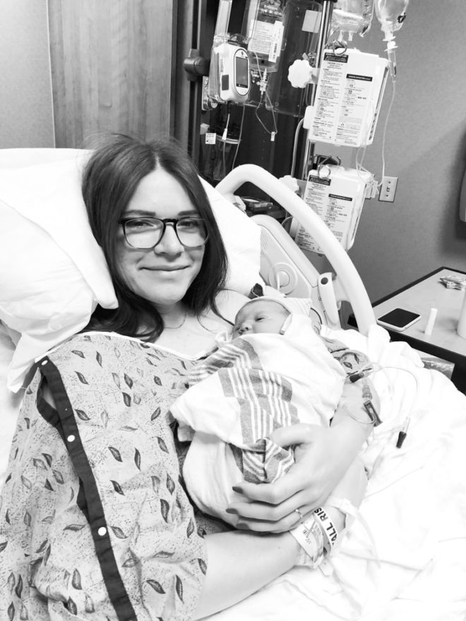 mother sitting up in hospital bed holding a swaddled newborn