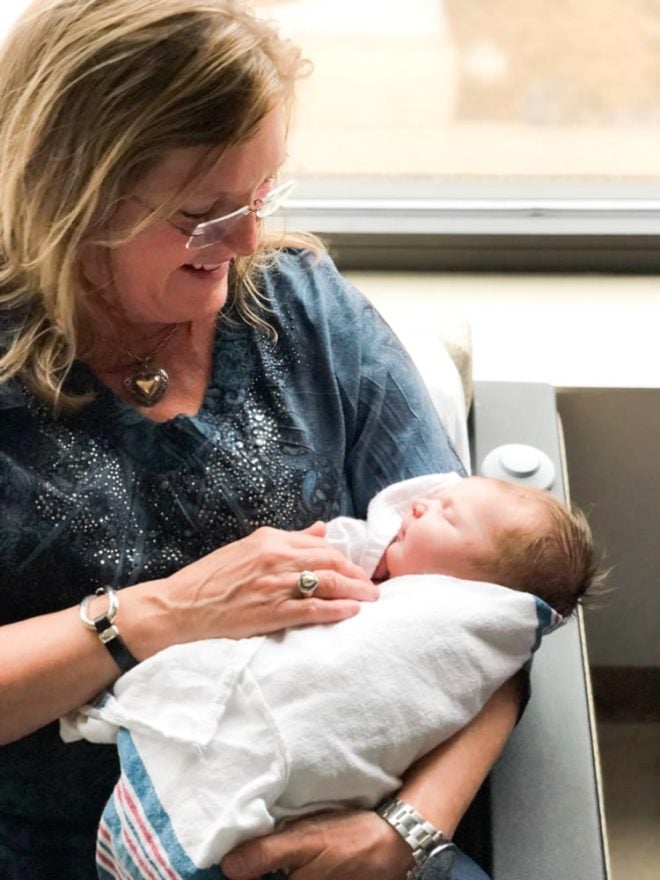 proud grandmother holds swaddled newborn and looks down smiling