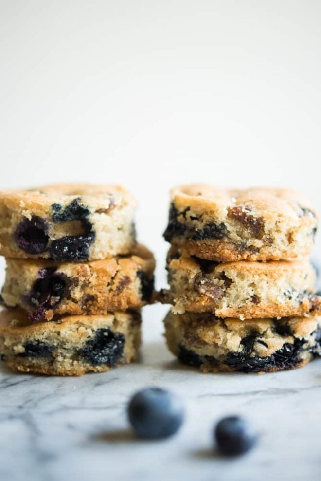 two stacks of blueberry sausage breakfast muffins on a white marbled table with fresh blueberries sprinkled around