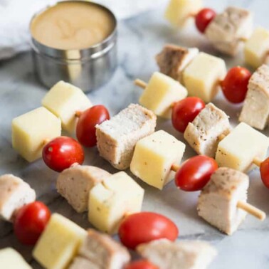overhead view multiple chicken skewers with cheese and tomatoes and honey mustard dipping sauce