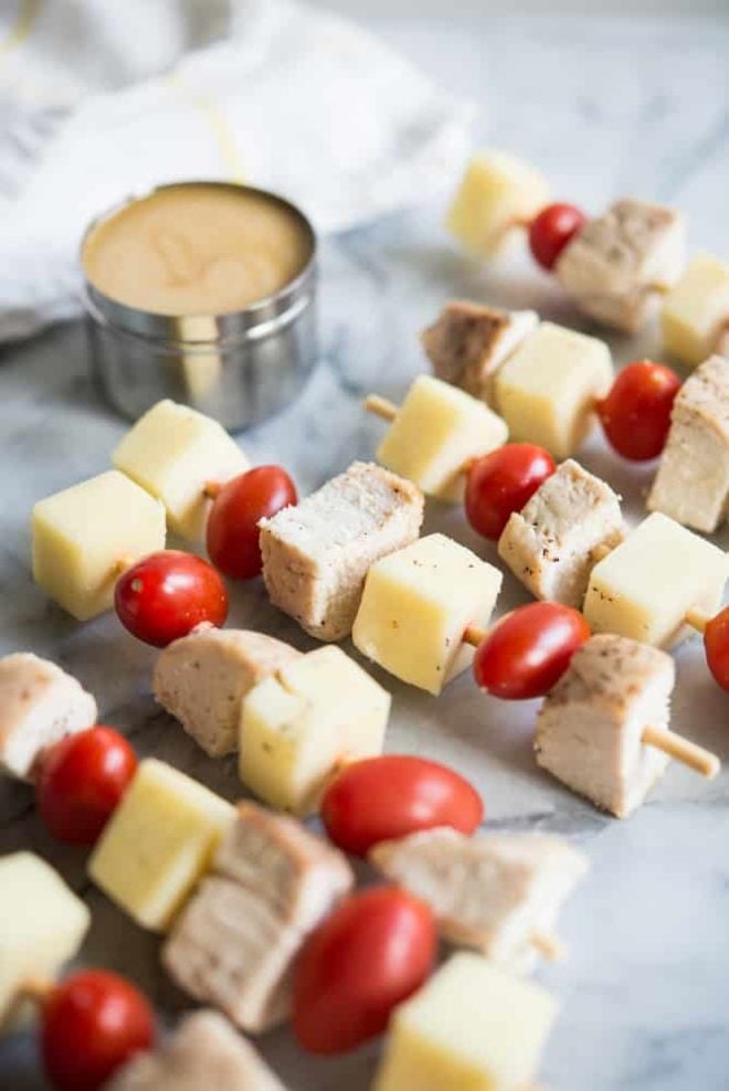 multiple chicken skewers with cheese and tomatoes and honey mustard dipping sauce