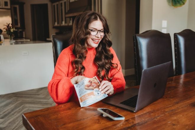 a woman with long dark hair working on her computer while eating beef snacks