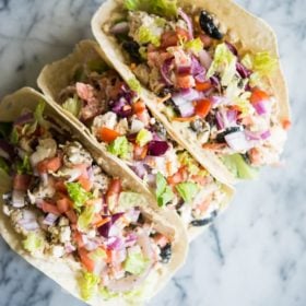 tortillas loaded with tomatoes, red onion, hummus, chicken, olives, and feta cheese (mediterranean hummus wraps) sitting on a marble surface