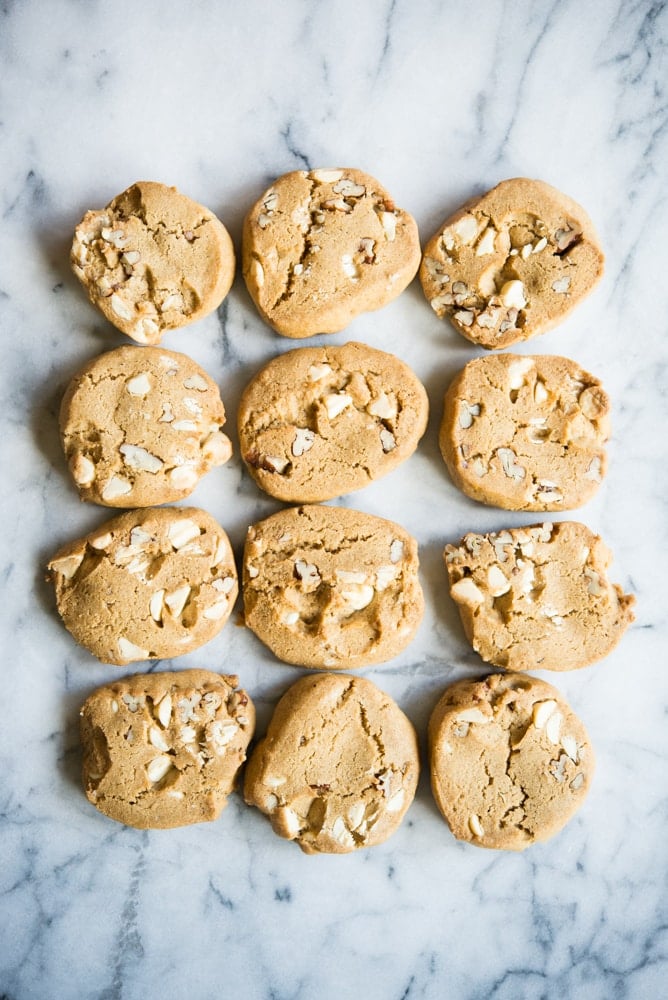 rows of pumpkin spice icebox cookies with a slightly orange coloring and white chocolate chips and pecans on a marble surface