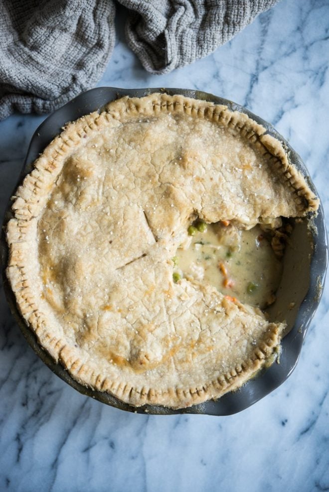 gluten free chicken pot pie with a scoop taken out of it so you can see peas and carrots in a grey deep dish pan on a marble surface