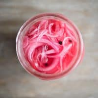 overhead view of a mason jar full of pink pickled red onions on a wooden table