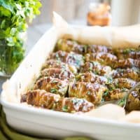 a white casserole dish filled with asian cabbage rolls and garnished with chopped cilantro