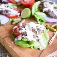 beef sliders on top of lettuce, red onion, and tomato slices with chipotle lime mayo drizzled on top