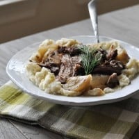 a white plate of Cinnamon and Fennel Braised Pork with a neutral plaid napkin on a grey wooden table