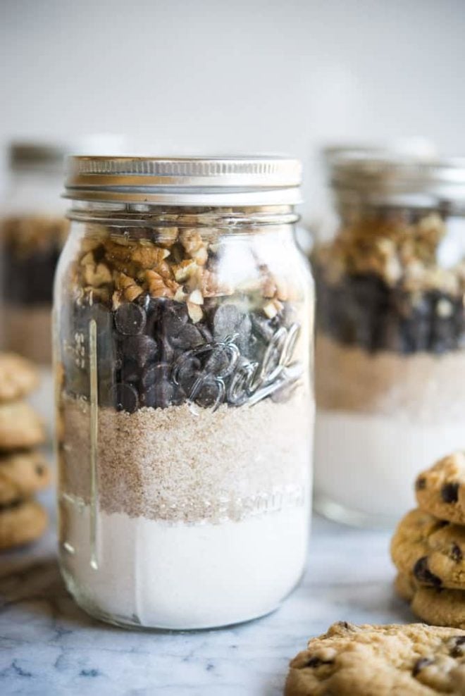 Gluten free chocolate chip cookie mix in mason jars on a marble slab surrounded by chocolate chip cookies