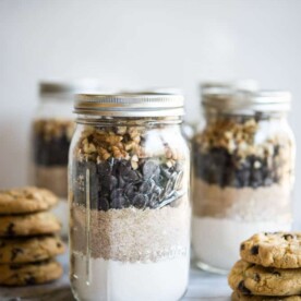 Gluten free chocolate chip cookie mix in mason jars on a marble slab surrounded by chocolate chip cookies