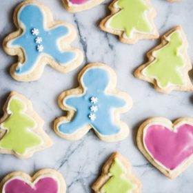 Top down view of sugar cookies cut out in the shapes of a gingerbread man, tree, and heart. All have been decorated with frosting.