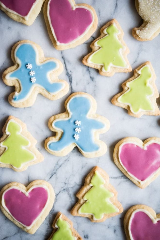 Top down view of sugar cookies cut out in the shapes of a gingerbread man, tree, and heart. All have been decorated with frosting.