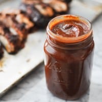 mason jar full of paleo barbecue sauce on a marble table with ribs blurred in the background