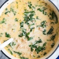 creamy kale and sausage soup in a blue pot on a marble background