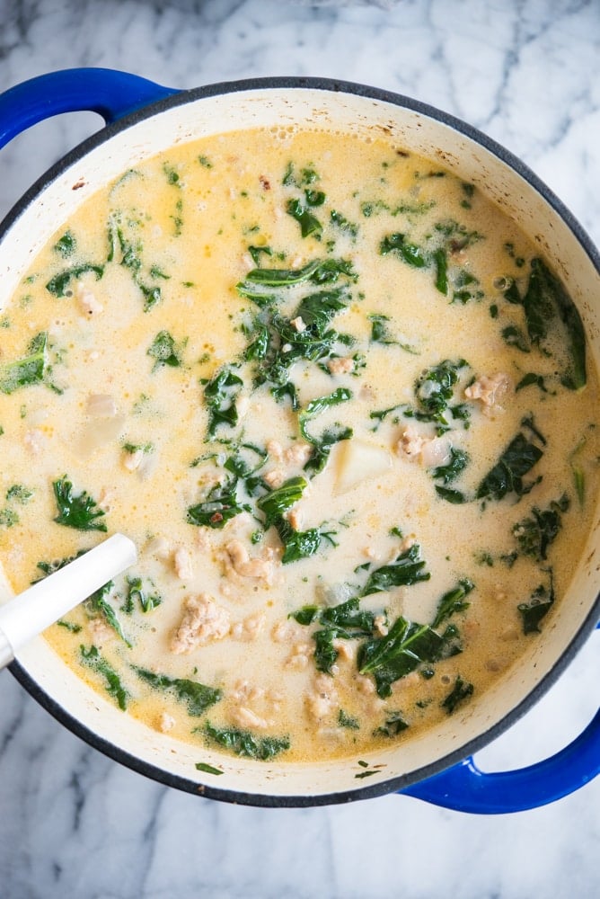 creamy kale and sausage soup in a blue pot on a marble background