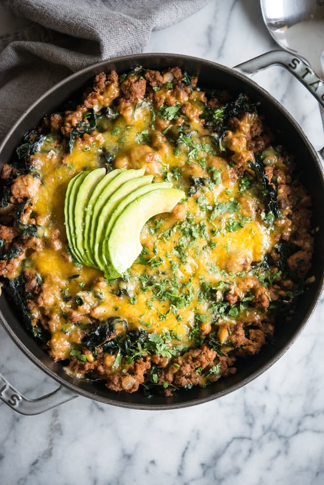 Beef taco casserole with avocado slices on top in a grey cast iron baking dish on a marble cutting board