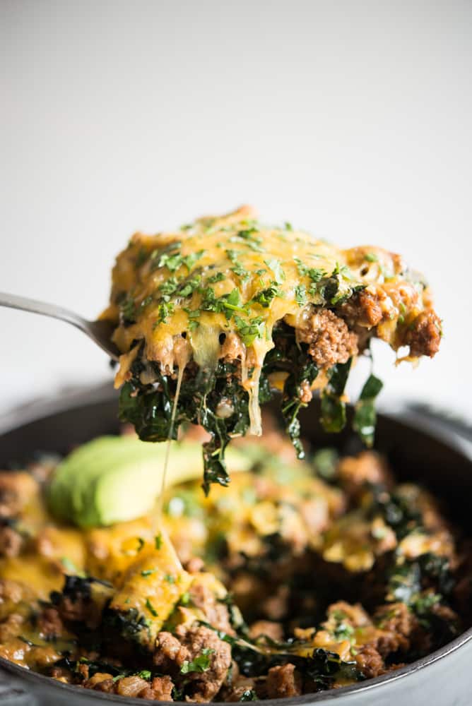 a spoon full of Beef taco casserole - you can see ground beef and shredded kale covered with melting cheese and chopped cilantro