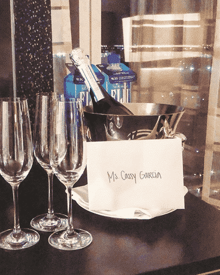 3 champagne glasses on a black table with a bottle of champagne chilled in an ice bucket and a card that reads Ms. Cassy Garcia