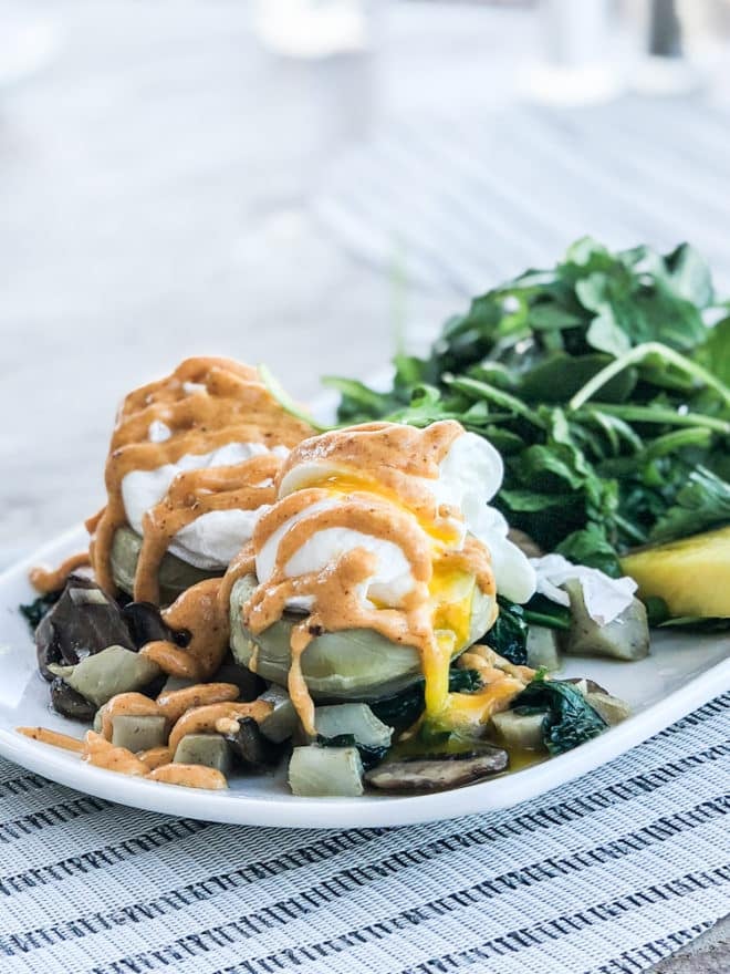 a breakfast hash plate with fried eggs and an orange sauce drizzled on top