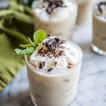 clear glasses filled with vegan baileys and topped with whipped cream, shaved chocolate, and mint leaves