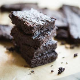 flourless dark chocolate brownies stacked on top of one another on top of parchment paper on a marble surface