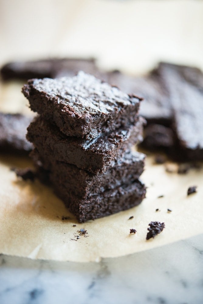 flourless dark chocolate brownies stacked on top of one another on top of parchment paper on a marble surface